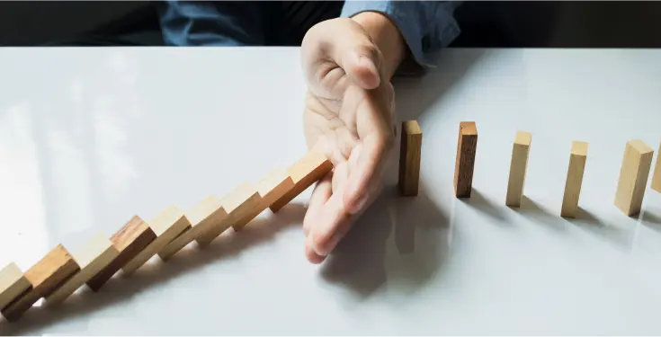 przewracające się domino, ręka, która je wstrzymuje